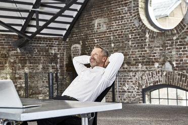 Lächelnder Geschäftsmann, der an einem Tisch in einem Loft sitzt und sich zurücklehnt - FMKF03665