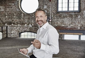 Porträt eines glücklichen Geschäftsmannes mit Tablet in einem Loft - FMKF03669