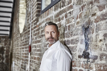 Portrait of businessman leaning against brick wall - FMKF03670