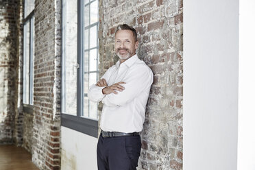 Portrait of confident businessman leaning against brick wall - FMKF03674