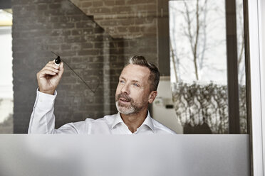 Businessman drawing on glass pane - FMKF03683