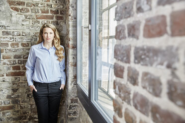 Portrait of confident businesswoman at brick wall - FMKF03690