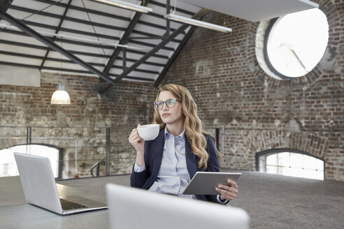 Geschäftsfrau mit Tasse Kaffee und Tablet am Tisch in einem Loft - FMKF03702