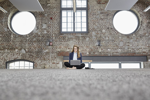 Barfüßige Geschäftsfrau, die auf dem Boden in einem Loft sitzt und einen Laptop benutzt, lizenzfreies Stockfoto