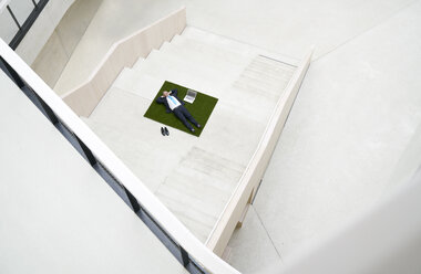 Top view of businesssman lying on stairs next to laptop - FMKF03711