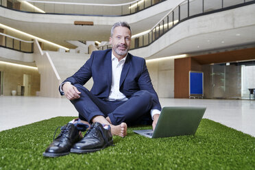 Businesssman sitting on synthetic turf using laptop - FMKF03718