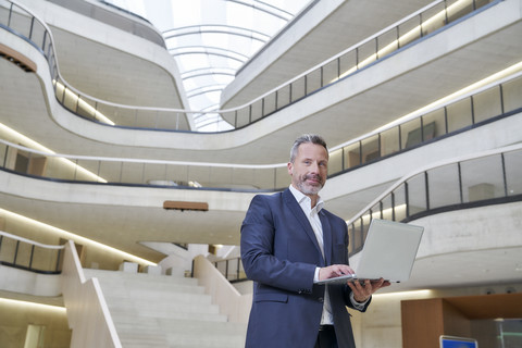 Geschäftsmann mit Laptop in einem modernen Bürogebäude, lizenzfreies Stockfoto