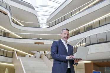 Geschäftsmann mit Laptop in einem modernen Bürogebäude - FMKF03719