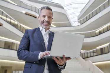 Businesssman using laptop in modern office building - FMKF03720