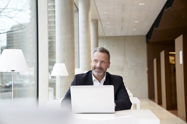 Smiling businesssman using laptop on table - FMKF03723