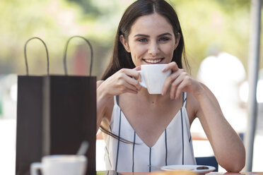 Smiling woman with shopping bag enjoying coffee at cafe - ZEF13393