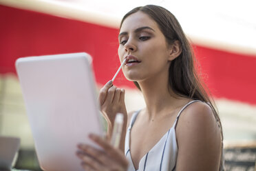 Young woman applying lip gloss holding digital tablet - ZEF13397