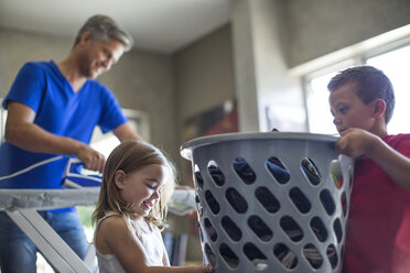 Zwei Kinder helfen ihrem Vater bei der Hausarbeit und tragen einen Wäschekorb - ZEF13437