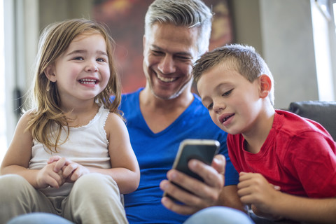 Glücklicher Vater mit Kindern, die sich ein Mobiltelefon teilen, lizenzfreies Stockfoto