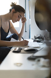 Junge Frau macht sich Notizen am Schreibtisch - KKAF00593