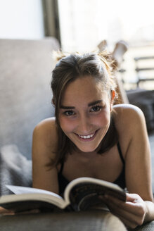 Lächelnde junge Frau in Unterwäsche liest ein Buch auf der Couch - KKAF00608