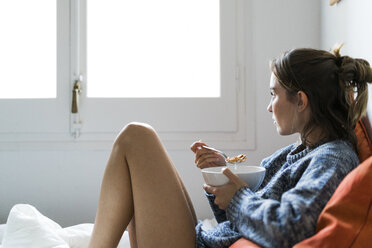 Serious young woman eating cereals in bed - KKAF00625