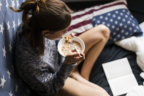 Draufsicht auf eine junge Frau, die Müsli isst und ein Buch liest - KKAF00627