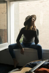 Laughing young woman wearing a hat sitting in window frame - KKAF00634