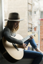 Junge Frau sitzt im Fensterrahmen und spielt Gitarre - KKAF00635