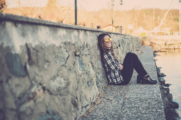 Frau sitzt im Freien und lehnt sich an eine Wand - SIPF01507