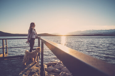 Frau am See beobachtet Sonnenuntergang mit ihrem Hund - SIPF01510