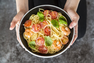 Hands holding bowl of spaghetti with prawns, tomatoes and basil - SARF03271