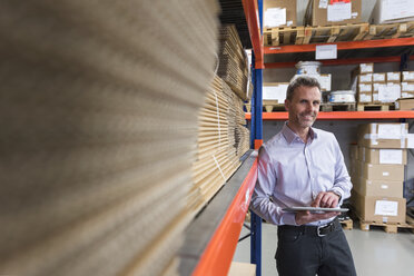 Smiling businessman with tablet in factory hall - DIGF01583