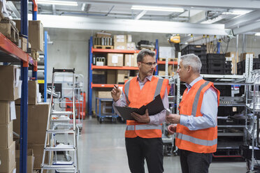 Two colleagues in factory hall wearing safety vests holding clipboard - DIGF01589