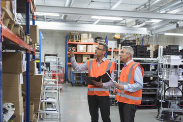 Two colleagues in factory hall wearing safety vests holding clipboard - DIGF01590