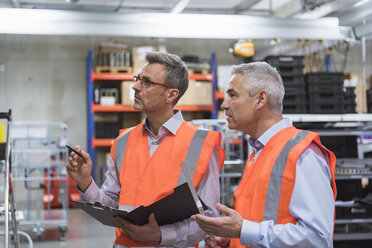 Two colleagues in factory hall wearing safety vests holding clipboard - DIGF01591