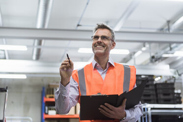 Man in factory hall wearing safety vest holding clipboard - DIGF01592