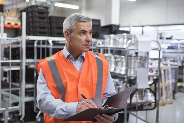 Man in factory hall wearing safety vest holding clipboard - DIGF01595