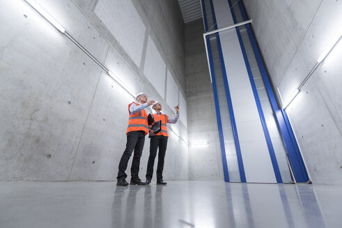 Two colleagues wearing safety vests and hard hats talking in a building - DIGF01600
