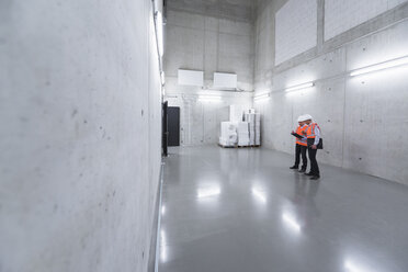 Zwei Kollegen mit Sicherheitswesten und Schutzhelmen unterhalten sich in einem Gebäude - DIGF01605