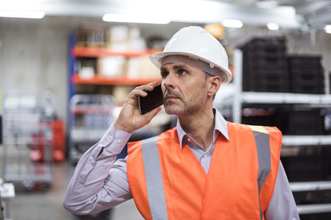 Man in factory hall wearing safety vest and hard hat talking on cell phone stock photo