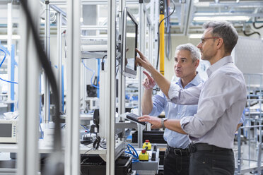 Two businessmen in modern factory hall talking at computer monitor - DIGF01616