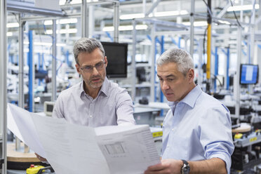 Zwei Geschäftsleute besprechen in einer Fabrikhalle einen Bauplan - DIGF01623