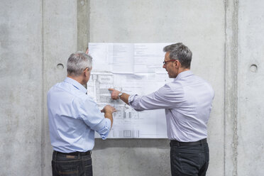 Zwei Geschäftsleute besprechen einen Bauplan an einer Betonwand - DIGF01625
