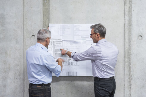 Two businessmen discussing construction plan at concrete wall - DIGF01625