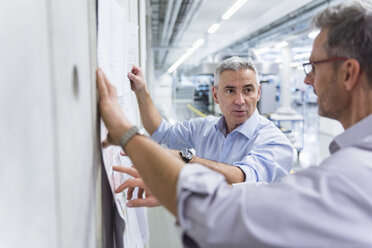 Two businessmen discussing construction plan at concrete wall - DIGF01628