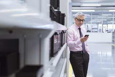 Manager in der Werkstatt einer Fabrik mit Smartphone - DIGF01655