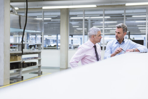 Zwei Manager diskutieren in der Fabrikhalle eines Unternehmens - DIGF01670