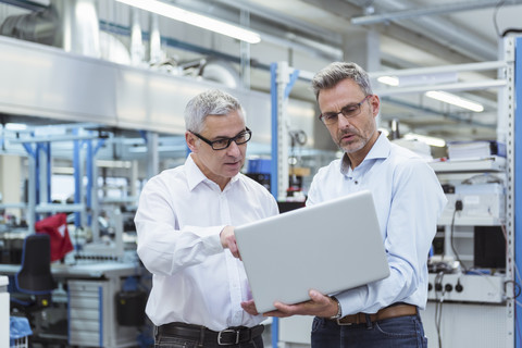 Zwei Manager stehen in der Firma und benutzen einen Laptop, lizenzfreies Stockfoto