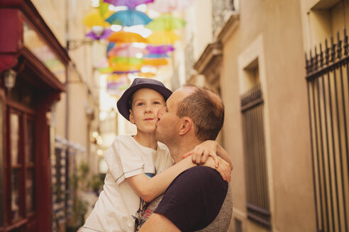 Frankreich, Languedoc, Beziers, Vater küsst Sohn mit bunten Regenschirmen im Hintergrund - NMSF00035