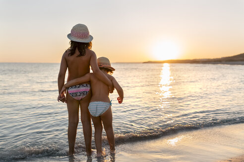 Spanien, Menorca, zwei Mädchen beobachten den Sonnenuntergang am Strand - MGOF03175