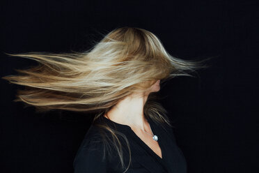 Junge blonde Frau, die ihr Haar vor einem schwarzen Hintergrund wirft - CHAF01805