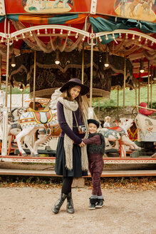Glückliche junge Frau und kleines Mädchen vor einem Kinderkarussell auf dem Jahrmarkt - CHAF01808