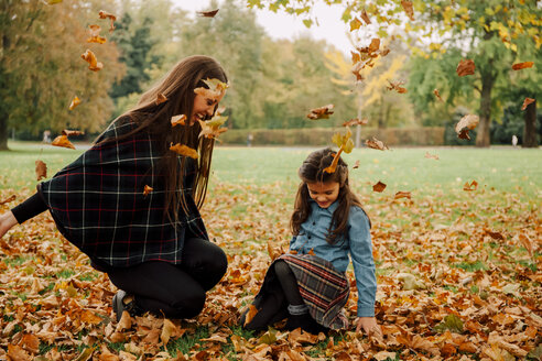 Junge Frau und kleines Mädchen spielen mit Herbstblättern auf einer Wiese - CHAF01812