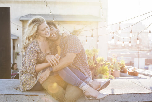 Happy couple sitting on rooftop, embracing each other - WESTF22827